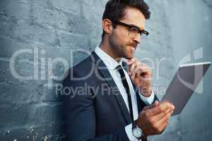 Big business decisions require careful planning. a handsome young businessman using his tablet while standing against a grey facebrick wall.