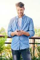 I wonder what my friends are up to. a confident young man texting on his cellphone outside during the day.