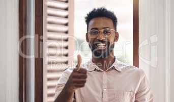 Thumbs up, endorsing and thank you with a young man smiling, feeling positive and giving his approval while standing inside. Portrait of a happy male wearing glasses and giving his trust or support