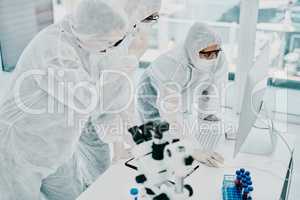 Group of doctors and scientists using computer for medical research on viruses dressed in hazmat suits, for coronavirus cure. Innovation researchers conducting experiment and waiting for test results