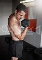 Making his bicep bulge. a handsome and muscular young man working out with a dumbbell in the gym.