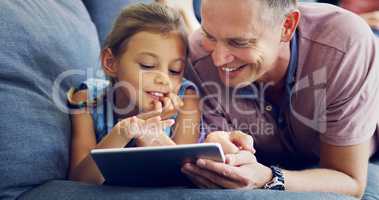 Learning about the ways of a wireless world. a cute little girl using a digital tablet with her father on the sofa at home.