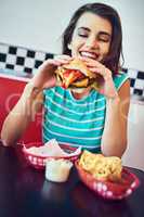 Grabbing a bite to eat. an attractive young woman enjoying a burger in a retro diner.