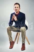 Sitting in the seat of success. Studio portrait of a confident young businessman sitting on a chair against a gray background.