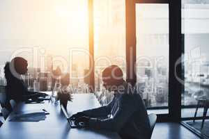 Silhouette, working and sitting in the city office to focus in the morning. Business, people and typing at the boardroom table at a calm time of day. Cityscape, window and flare view of urban life.