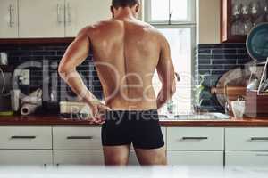 Alright time to kick things into gear. Rearview shot of a muscular young man standing in his underwear while preparing food in the kitchen at home.