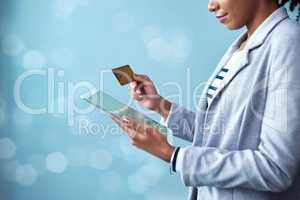 Credit card for online banking, shopping and buying on tablet while standing alone isolated on blue copy space. African female paying for purchase with fintech technology on blue bokeh background
