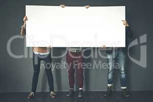 Group of businesspeople holding up a copyspace sign voicing their opinion at work with a grey background. People with blank poster advertising, marketing and express or convey important messages