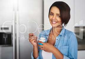 My healthy mid morning snack. an attractive young woman eating a tub of yoghurt at home.