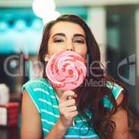 Im a candy kinda girl. Cropped portrait of an attractive young woman eating a giant lollipop in a retro diner.