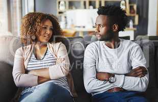 Unhappy couple talking about a breakup or problems in their relationship while sitting on a sofa at home together. Boyfriend and girlfriend frustrated by issues, arguing and angry after a fight