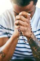 He hears all your prayers. a young man holding his rosary while praying.
