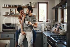 Happy, in love and laughing while an interracial couple enjoys morning coffee and bonding while having good communication in a relationship. Husband and wife talking while standing in kitchen at home