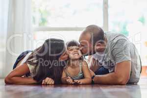 Lots of kisses for their little one. Portrait of a mother and father bonding with their adorable young daughter at home.