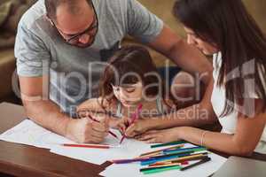 Creative expressions is important to this family. a mother and father drawing together with their young daughter at home.