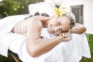 One has to spoil themselves now and then. Portrait of a relaxed middle aged woman lying on a massage bed with warm stones on her back at a spa during the day.