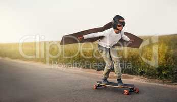 Hes got the wildest imagination. a young boy pretending to fly with a pair of cardboard wings while riding a skateboard outside.