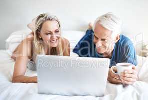 Time for some leisurely browsing. a mature couple using a laptop while relaxing on their bed at home.