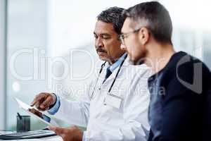 You see this is what my reports are telling me. a confident mature male doctor seated at his desk while consulting a patient inside a hospital during the day.