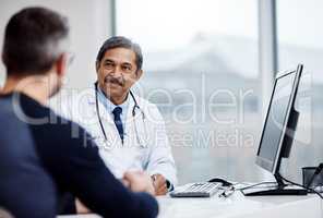 Always here to give you the best medical advise. a cheerful mature male doctor seated at his desk while consulting a patient inside a hospital during the day.