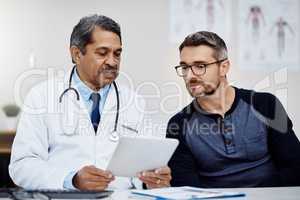 Lets have a look at the diagnostics. a confident mature male doctor seated at his desk while consulting a patient inside a hospital during the day.