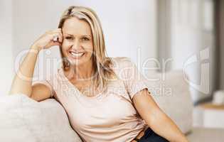 Happy, cheerful and smiling mature woman relaxing on the couch at home and enjoying her free time. Portrait of a beautiful housewife feeling content and comfortable while spending time alone