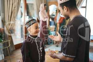 Muslim father and son talking and bonding in the living room during a religious holiday at home. Cute, smiling and happy Islamic boy listening to advice from his dad while wearing traditional outfit