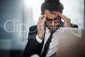 I cant focus at all. a young businessman suffering with a headache while working in an office.