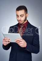 Technology can be a helpful tool in business. Studio shot of a handsome young businessman using a tablet against a grey background.