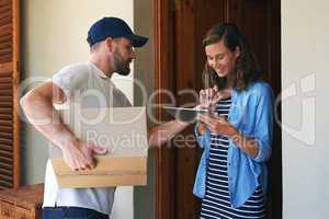 Sign just here please. a young woman using a digital tablet to sign for her delivery from the courier.