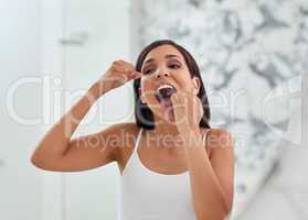 Im going to have the healthiest smile after this. an attractive young woman flossing her teeth in the bathroom.