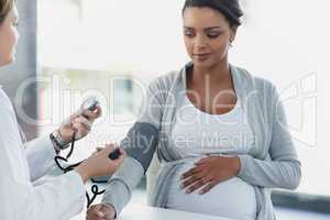 Time to check your blood pressure. a confident female doctor checking the blood pressure of a pregnant patient at a hospital during the day.