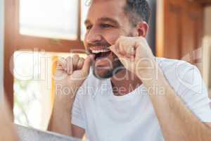 Take your dental hygiene routine a step further by flossing. a handsome young man flossing his teeth in the bathroom.