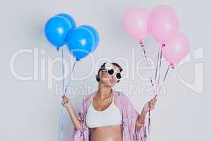 Will it be a girl or a boy. Studio shot of a beautiful young pregnant woman holding blue and pink balloons against a gray background.
