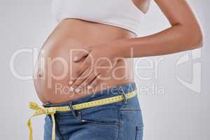 Inching closer to her due date. Cropped studio shot of a pregnant woman wearing jeans and a tape measure against a gray background.