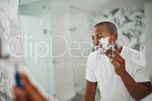 Hes not a fan of the face fuzz. a handsome young man shaving his facial hair in the bathroom.