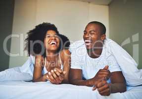 Laughter turns a good morning into a great morning. a happy young couple relaxing under a duvet in their bedroom.