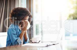 I just hate getting sick, especially at this time. Portrait of a young woman blowing her nose with a tissue while working at home.