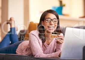 Shes the first to scoop up the latest deals. an attractive young woman using a laptop and credit card on the sofa at home.