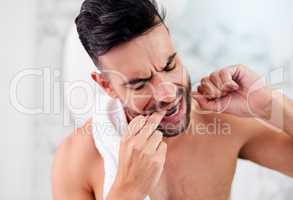 Be careful not to floss too vigorously to prevent dental damage. a handsome young man flossing his teeth in the bathroom.