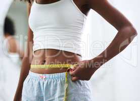 Knocking off the inches. Closeup shot of an unrecognizable woman measuring her waist.