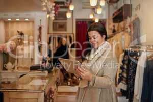 Managing her business with the help of technology. an attractive mature female entrepreneur working on a tablet in her self-owned boutique.