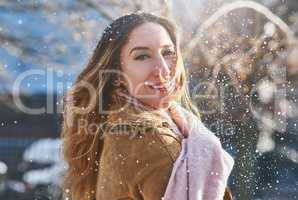 The snowflakes fall like glitter in the light. an attractive young woman enjoying being out in the snow.