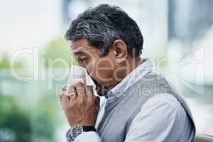 Flu season is once again upon us. a mature man blowing his nose.