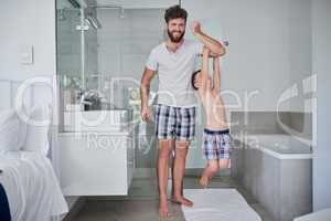 We have tons of fun, from morning till night. a little boy hanging on his fathers arm in the bathroom at home.