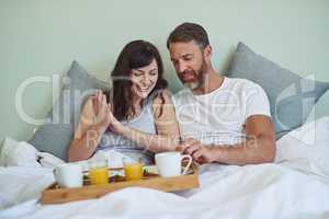 Lets dig in. a cheerful young couple sitting in bed while enjoying breakfast together during morning hours.
