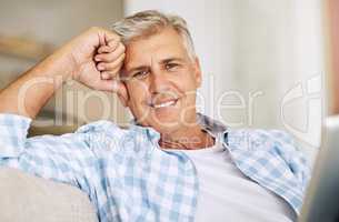 Mature man relaxing, smiling and sitting on his sofa at home on vacation. Older guy comfortable on couch, cheerful and reading at home while on holiday. Happy, retired male enjoying his leisure time.