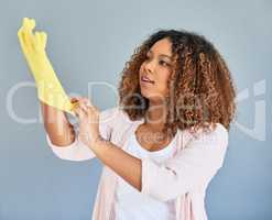 Getting her gloves on, time to get cleaning. Studio shot of a young attractive woman putting on rubber gloves against a gray background.