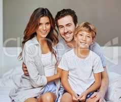 Cheerful happy family at any time of the day. Portrait of a cheerful young family seated on bed while holding each other and looking at the camera at home in the morning.