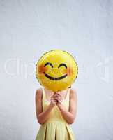 Keep smiling. Studio shot of an unrecognizable woman holding a smiling emoticon balloon in front of her face against a grey background.